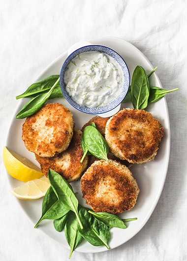 Tuna and potato patties served with spinach and greek yogurt on a light background, top view