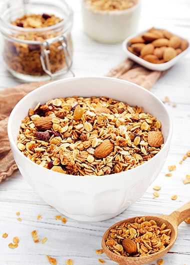 Tasty granola in bowls and spoon on white wooden background