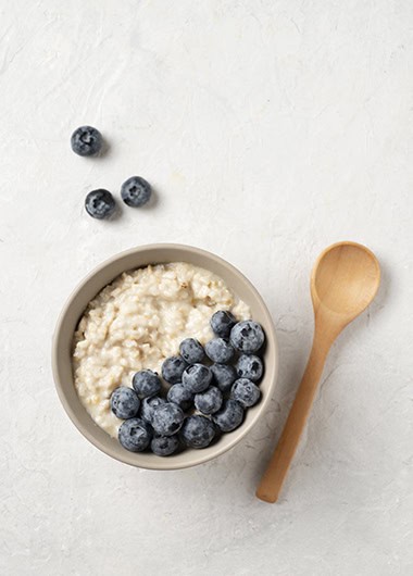 Oatmeal porridge with blueberries in bowl with wooden spoon. Top view