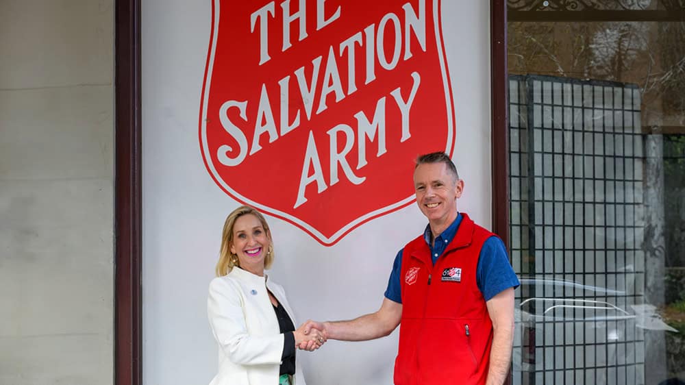 Diabetes Australia Group CEO Justine Cain and Salvation Army spokesperson Brendan Nottle shake hands outside the Melbourne Salvation Army building and logo.